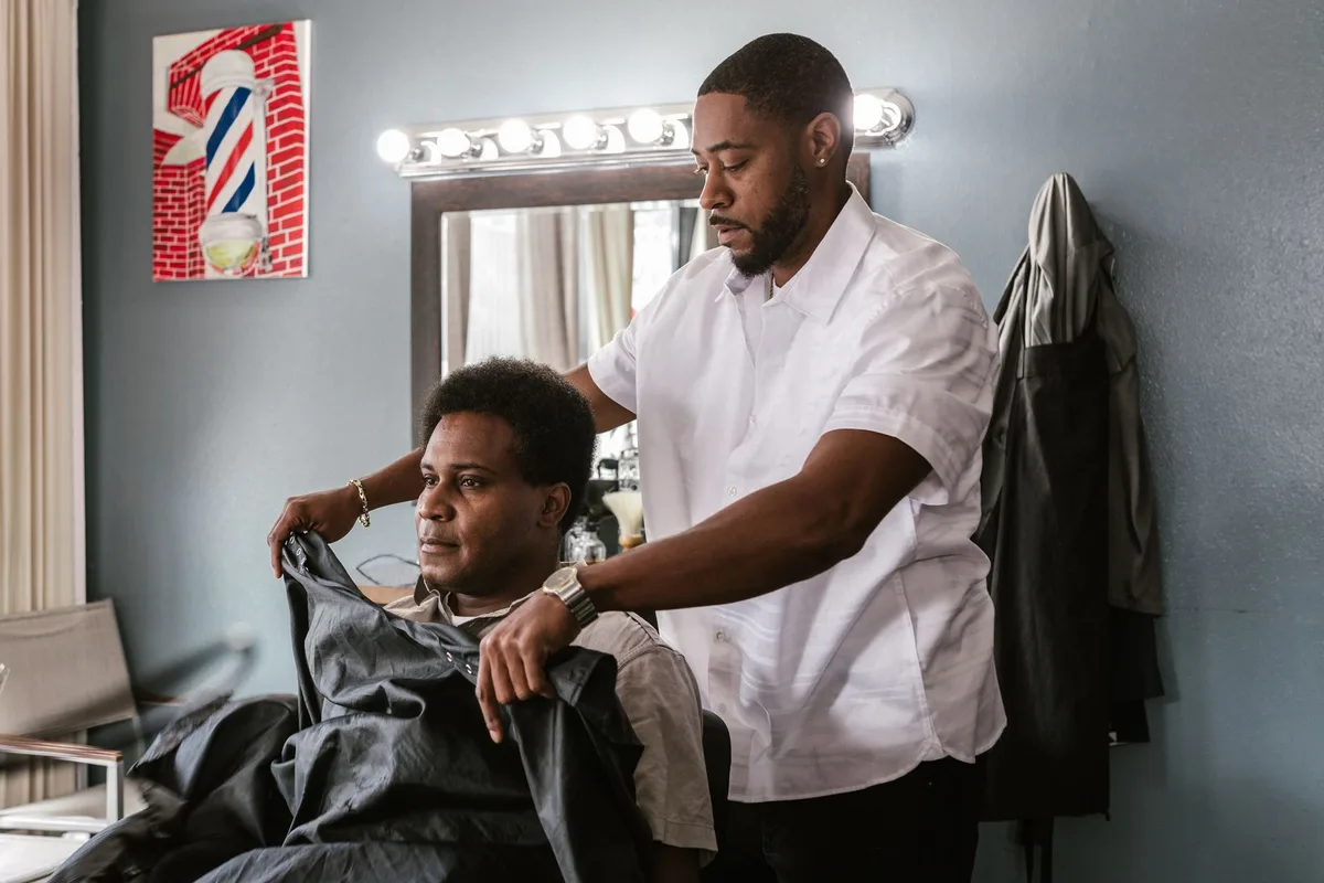Barbier qui pose la cape sur un client installé au fauteuil, le moment où l'habitué d'un barbershop peut fixer sa prochaine coupe