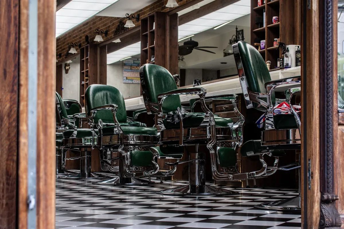 Row of green barber chairs in a salon with a checkered floor, like stations to rent out or to staff with commission stylists