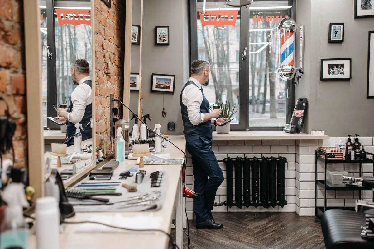 Barber alone in his barbershop, device in hand, between two appointments