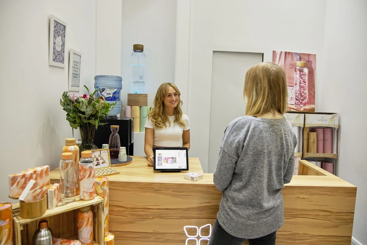 Cliente au comptoir d'un salon, devant l'écran de paiement tourné vers elle