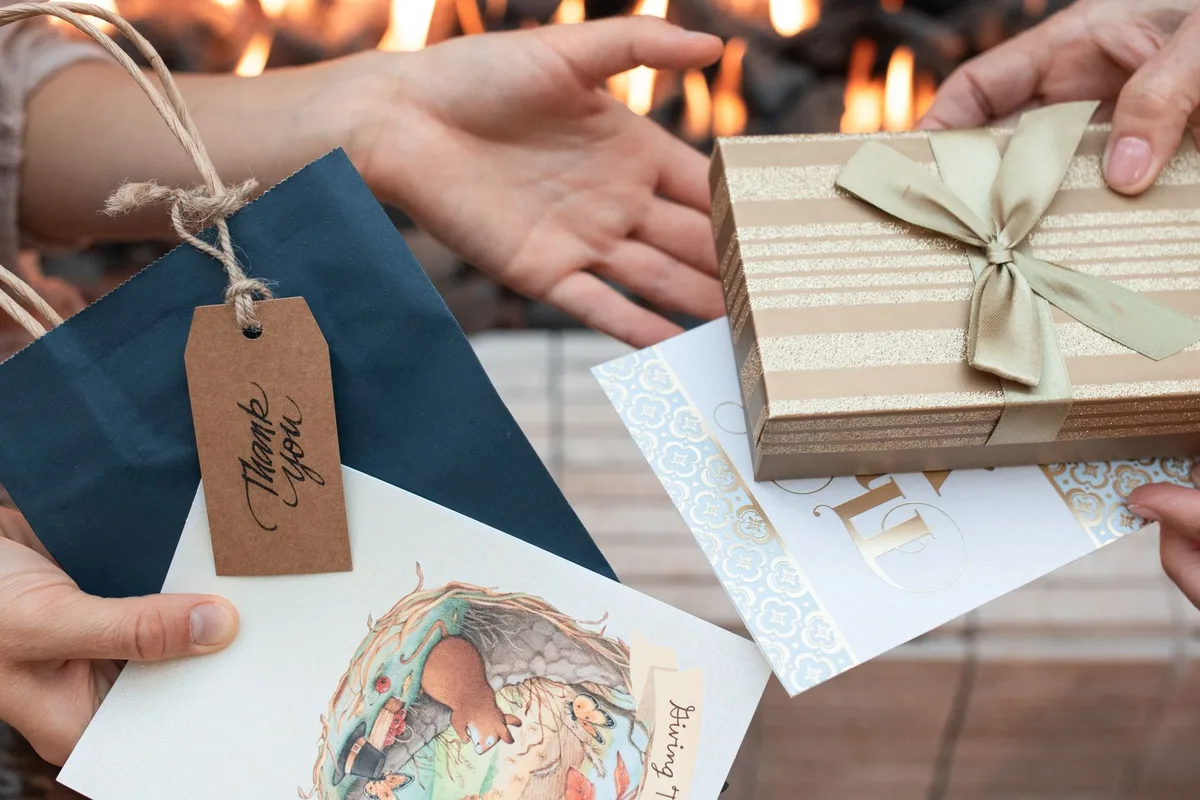 Hands exchanging a gift box, a bag and cards in front of a fireplace, like a salon gift card given over the holidays